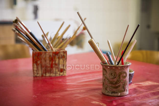 Tasse avec pinceaux et outils sur table — Photo de stock