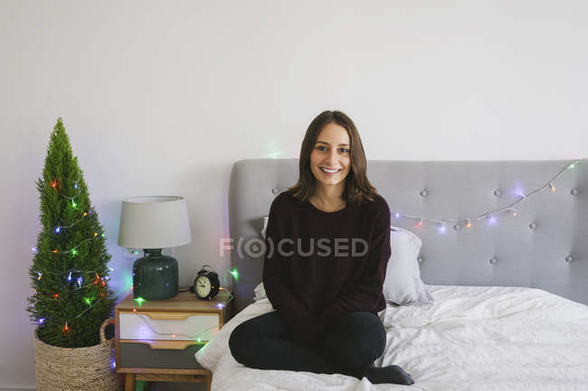 Портрет усміхається жінка, сидячи на ліжку, на Різдво — стокове фото