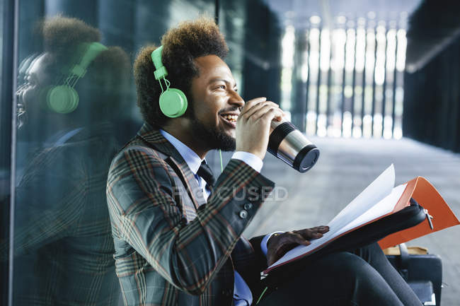 Lächelnder junger Geschäftsmann mit Coffee-to-go-Becher, Kopfhörer und Ordner im Freien — Stockfoto