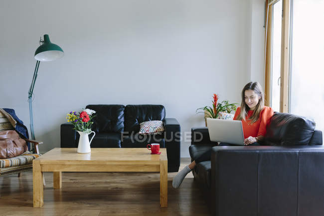 Молода жінка з ноутбуком розслабляючий на дивані у своїй вітальні — стокове фото