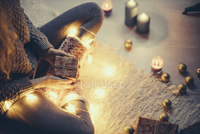 Donna seduta con regalo di Natale e luci fatate sul tappeto — Foto stock