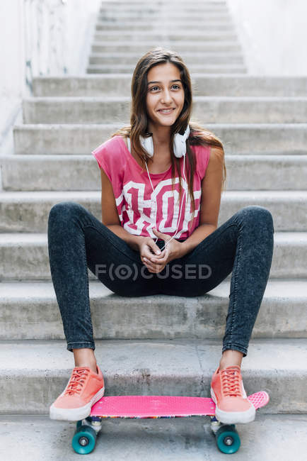Portrait of teenage girl sitting on stairs with a skateboard and  headphones — Stock Photo