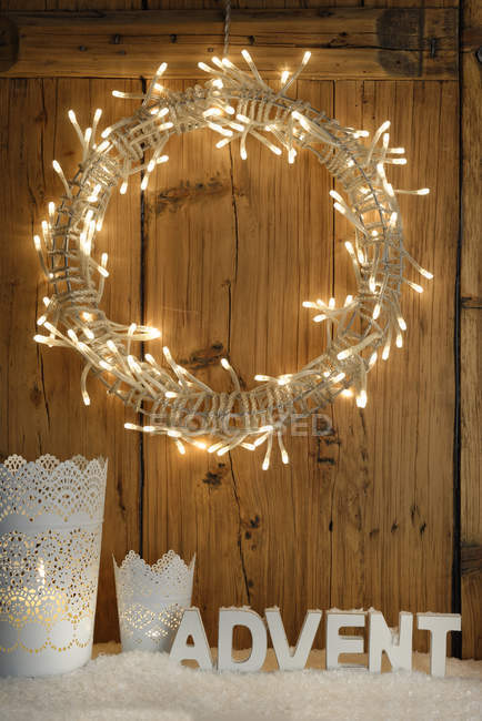 Decoración blanca con corona de Adviento iluminada frente a la pared de madera - foto de stock