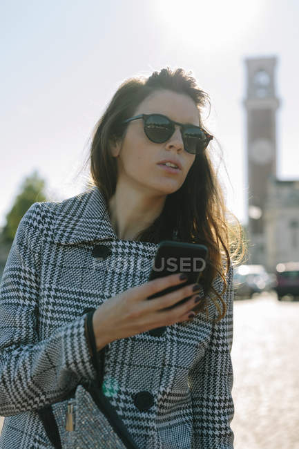 Woman wearing checkered coat and sunglasses holding cell phone — Stock Photo