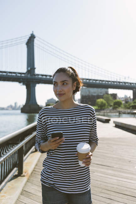 USA, New York City, portrait of smiling young woman with smartphone and coffee to go — Stock Photo