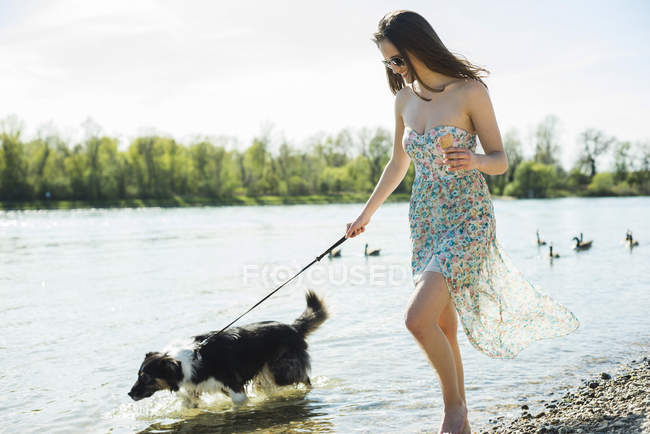 Young woman walking with dog at riverside — Stock Photo