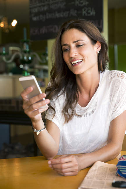 Portrait de femme souriante regardant son smartphone dans un café — Photo de stock