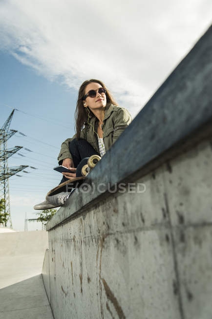 Woman with skateboard sitting on wall — Stock Photo
