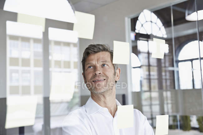 Uomo d'affari con appunti appiccicosi su vetro in ufficio — Foto stock