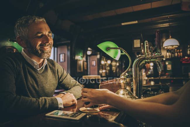 Uomo sorridente seduto al bancone di un pub — Foto stock
