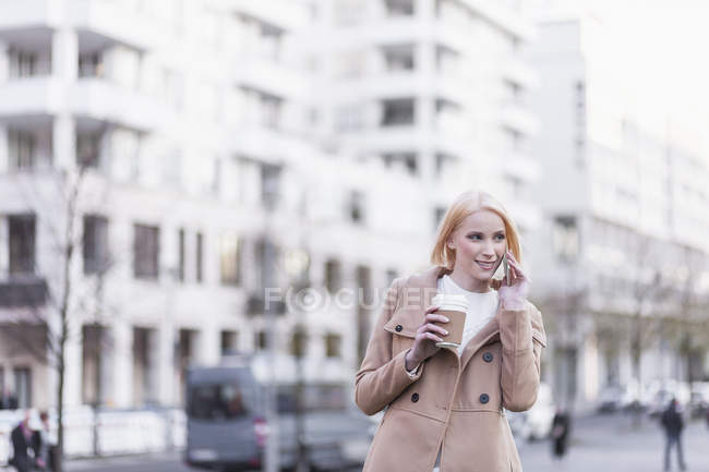 Mujer joven con café para ir a telefonear con smartphone - foto de stock