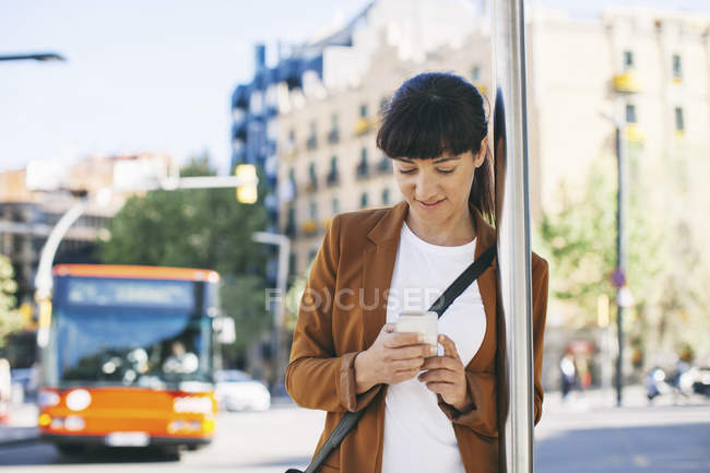 Geschäftsfrau mit Smartphone wartet an Bushaltestelle — Stockfoto