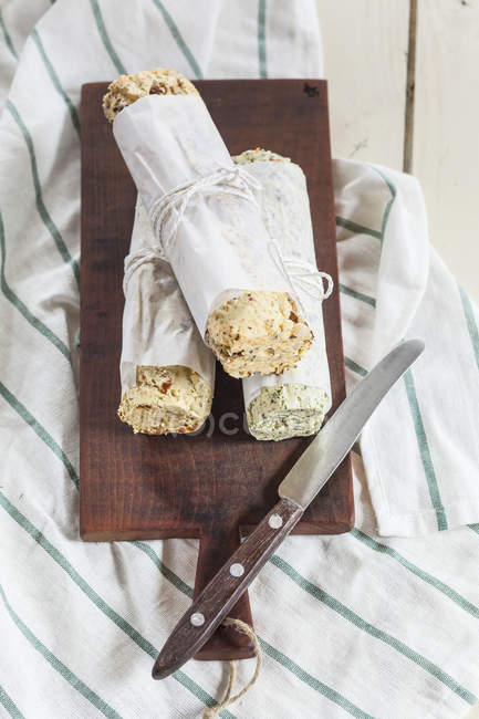 Trois rouleaux de beurres composés aux saveurs différentes sur planche à découper — Photo de stock