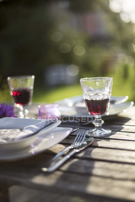 Gedeckter Gartentisch mit zwei Gläsern Rotwein im Gegenlicht — Stockfoto