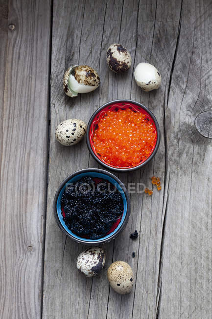 Caviale nero e rosso in ciotole, uova di quaglia sode su legno — Foto stock