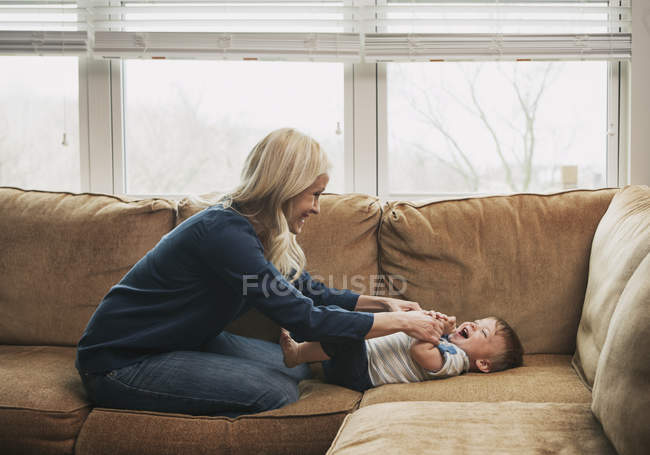Mère chatouillant tout-petit fils tout en étant assis sur le canapé — Photo de stock