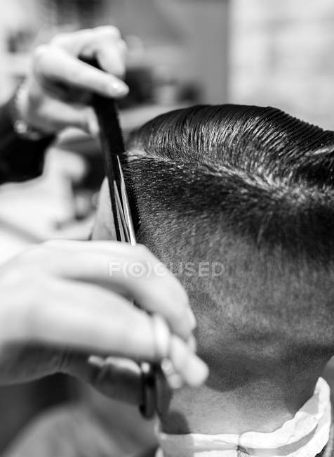 Peluquería cortando el pelo de un joven en una peluquería - foto de stock