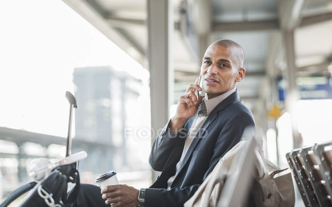 Uomo d'affari alla stazione ferroviaria che parla su smartphone — Foto stock