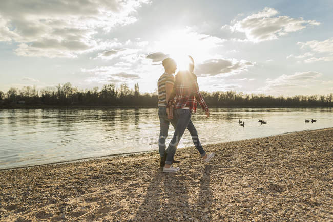 Joyeux jeune couple au bord de la rivière marchant main dans la main — Photo de stock