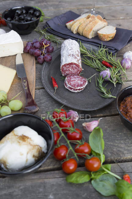 Variety of Italian antipasti over wooden surface with bowls and towel — Stock Photo