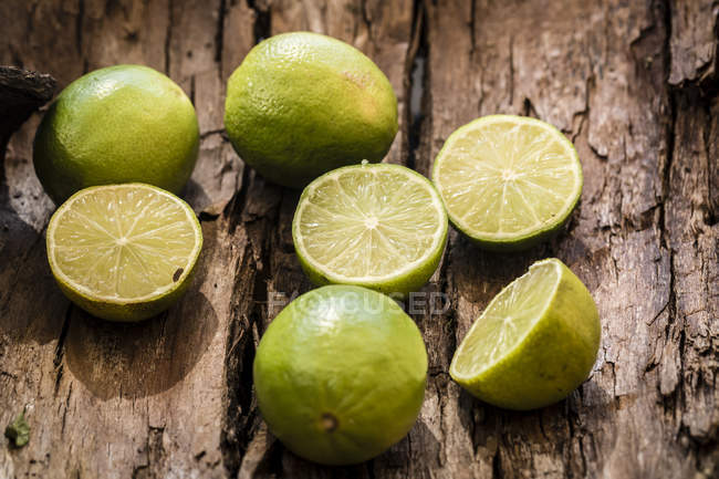 Citrons verts frais coupés en deux et entiers sur écorce de bois — Photo de stock