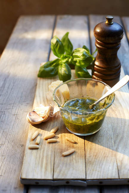 Bicchiere di pesto di basilico fatto in casa, ingredienti e un macinapepe sul tavolo di legno — Foto stock