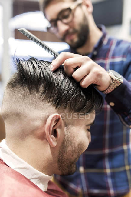 Парикмахер бреет волосы молодого человека в парикмахерской — стоковое фото