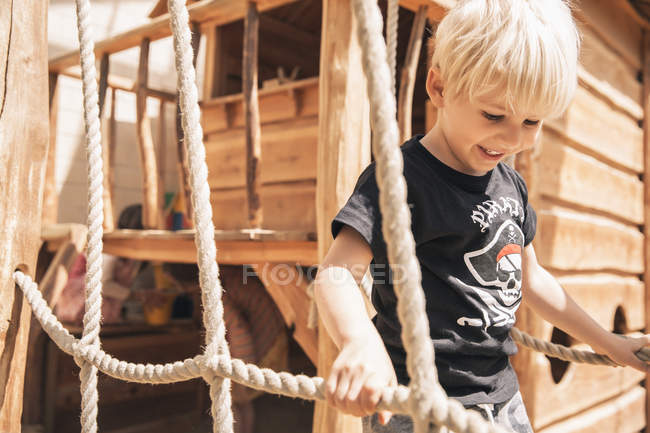 Smiling little boy walking along hanging bridge of wooden ship on playground — Stock Photo
