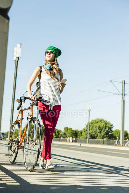 Mujer joven con bicicleta en el pavimento sosteniendo el teléfono celular - foto de stock
