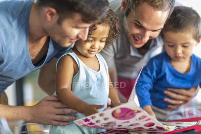 Due uomini con due bambini che guardano il libro delle foto — Foto stock