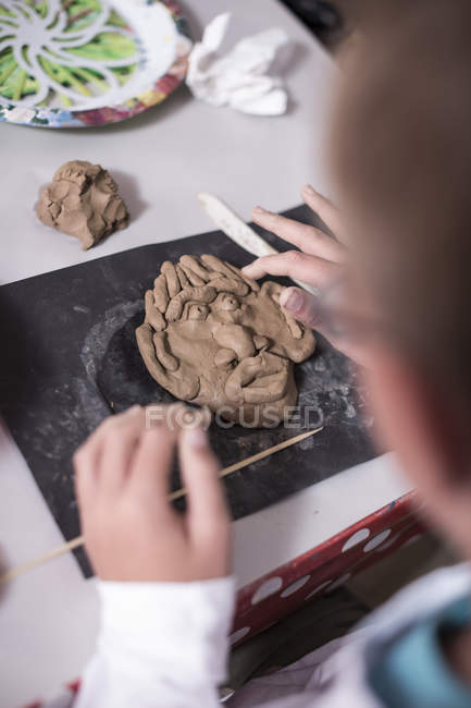 Boy making face from modeling clay in art class at school — Stock Photo