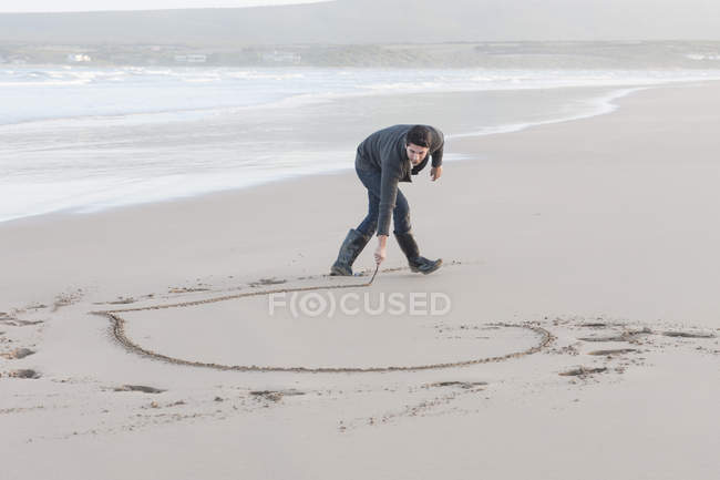 Mann kratzt Herz im Sandstrand an schöner Natur — Stockfoto