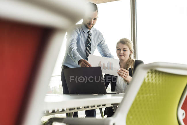 Joven hombre de negocios y mujer de negocios en sala de conferencias con ordenador portátil y diagrama - foto de stock