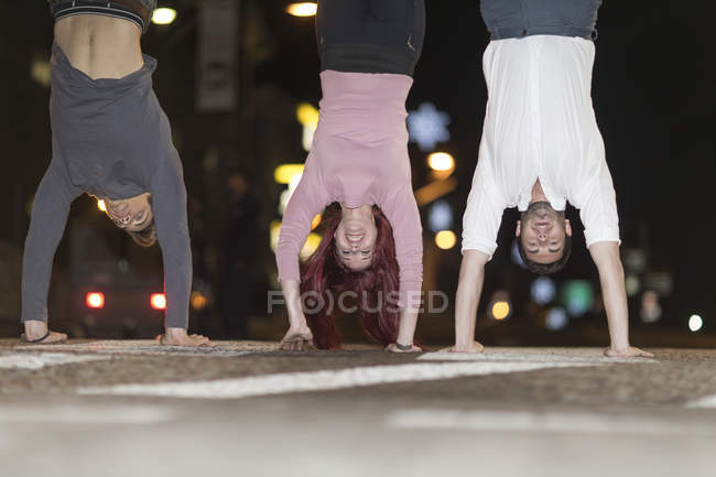 Three friends doing handstands on pavement at night — Stock Photo