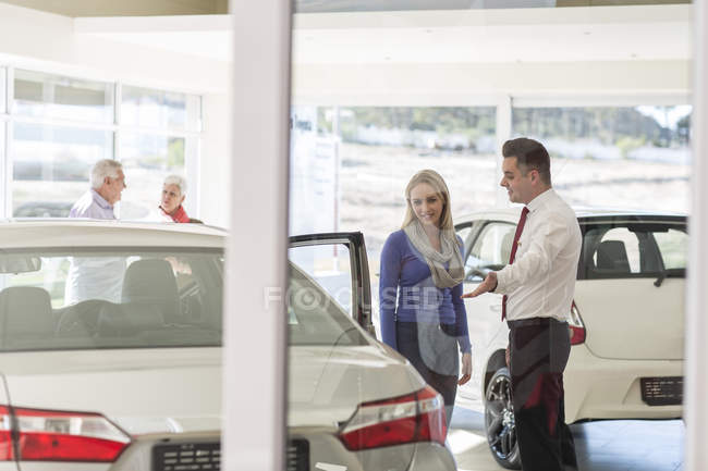 Rivenditore di auto che parla con una donna nello showroom — Foto stock