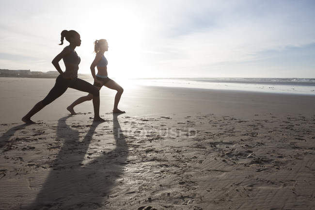 Deux femmes faisant des exercices d'étirement sur la plage au contre-jour — Photo de stock