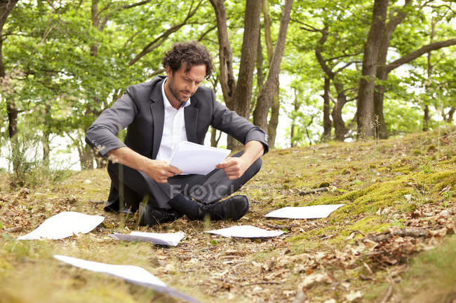 Geschäftsmann sitzt im Wald und liest Dokumente — Stockfoto