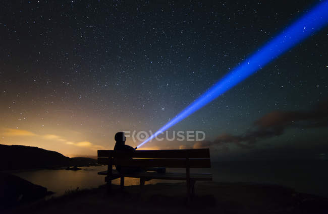 Espagne, Ortigueira, Loiba, silhouette d'un homme assis sur un banc sous un ciel étoilé avec un rayon bleu — Photo de stock