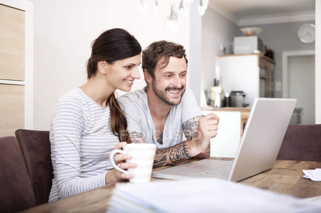 Lächelndes Paar sitzt am Holztisch und blickt auf Laptop — Stockfoto