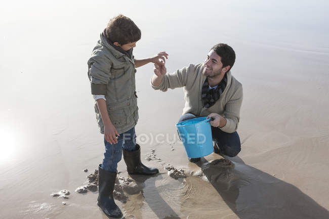 Padre e hijo jugando con arena en la playa - foto de stock