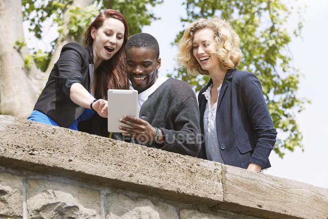Cheerful friends sharing digital tablet in city — Stock Photo
