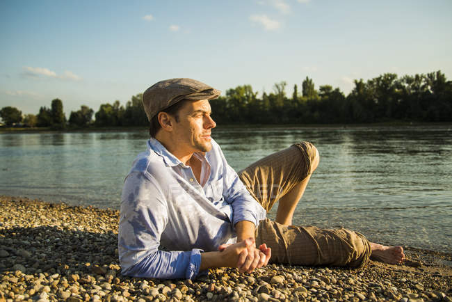 Man wearing cap relaxing at riverside in the evening twilight — Stock Photo