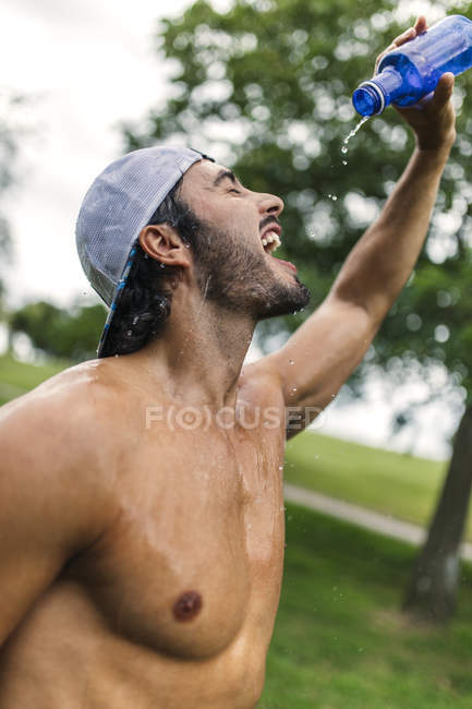 Athletic young man refreshing after training in the park — Stock Photo