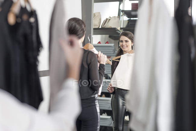 Donna che tiene il top guardando nello specchio in una boutique — Foto stock