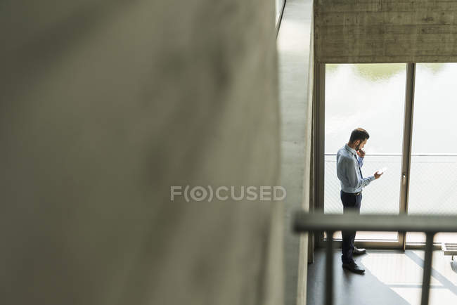 Jungunternehmer schaut aufs Handy am Fenster — Stockfoto