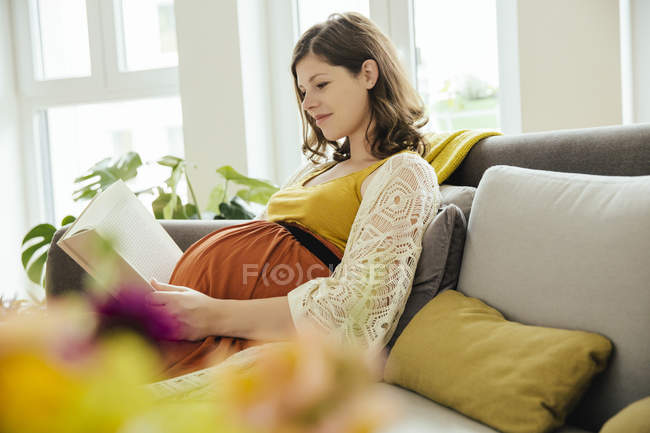 Pregnant Woman Reading A Book While Relaxing On Couch At Home