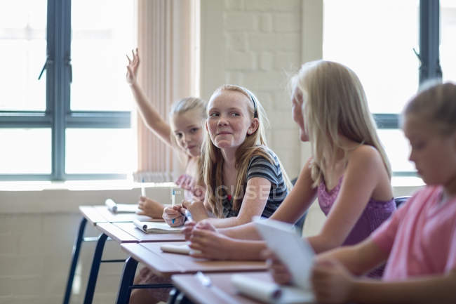 Schoolgirl in classroom with girls raising hand — Stock Photo