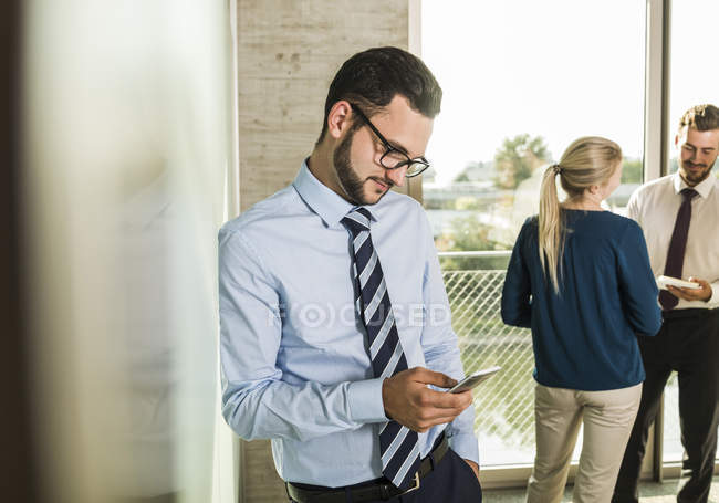 Empresario usando smartphone con colegas en segundo plano - foto de stock