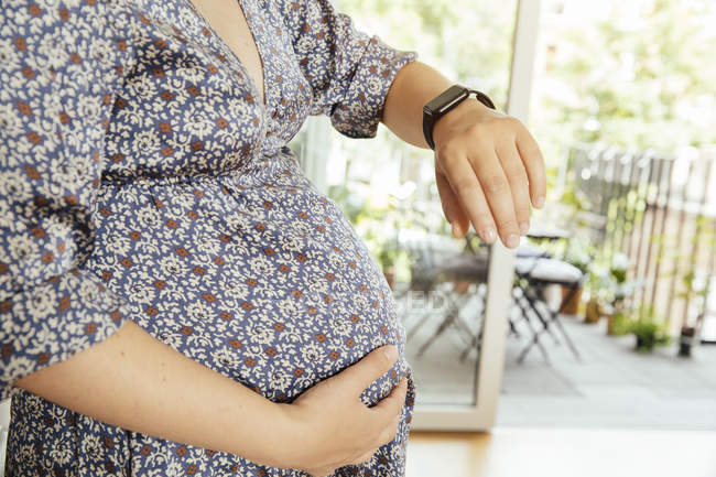 Беременная женщина смотрит на свои умные часы крупным планом — стоковое фото