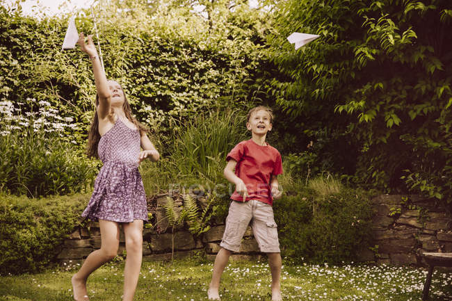 Chica y niño jugando con aviones de papel en el jardín - foto de stock
